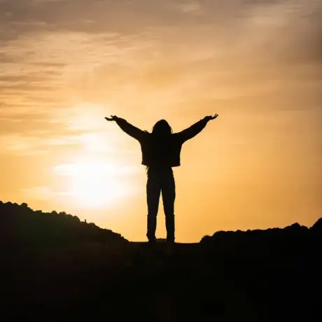 A silhouette of a joyful person against sunset light